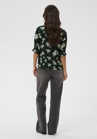 Tamsiai žalia gėlių bliuska su trumpomis, suvoliotomis rankovėmis, derinama su pilkais plačiais džinsais. Lygus audinys su subtiliu gėlių raštu.