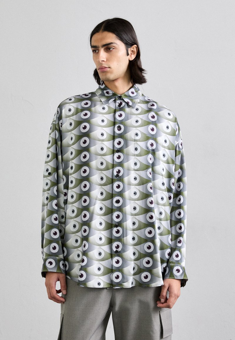 Chemise à manches longues vert pâle et gris, présentant un motif d'yeux avec des accents noir et blanc. Fabriquée dans un tissu lisse et brillant.