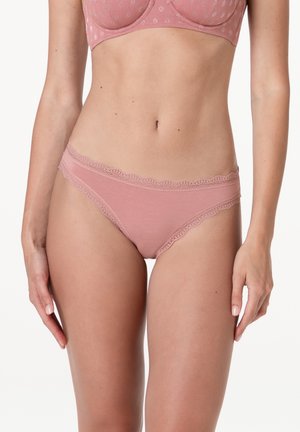 Donna che indossa un reggiseno rosa con motivo floreale e mutandine abbinate con bordi in pizzo, in piedi con le braccia rilassate lungo i fianchi su sfondo bianco.