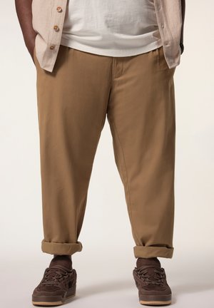 Khaki pants with a relaxed fit, cuffed at the ankles, made from a smooth fabric. Paired with dark brown lace-up shoes.