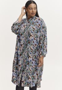Sukienka koszulowa w kwiaty, z mieszanką niebieskich, zielonych i beżowych odcieni na brązowym tle, z zapięciem na guziki i luźnym, oversize'owym krojem.