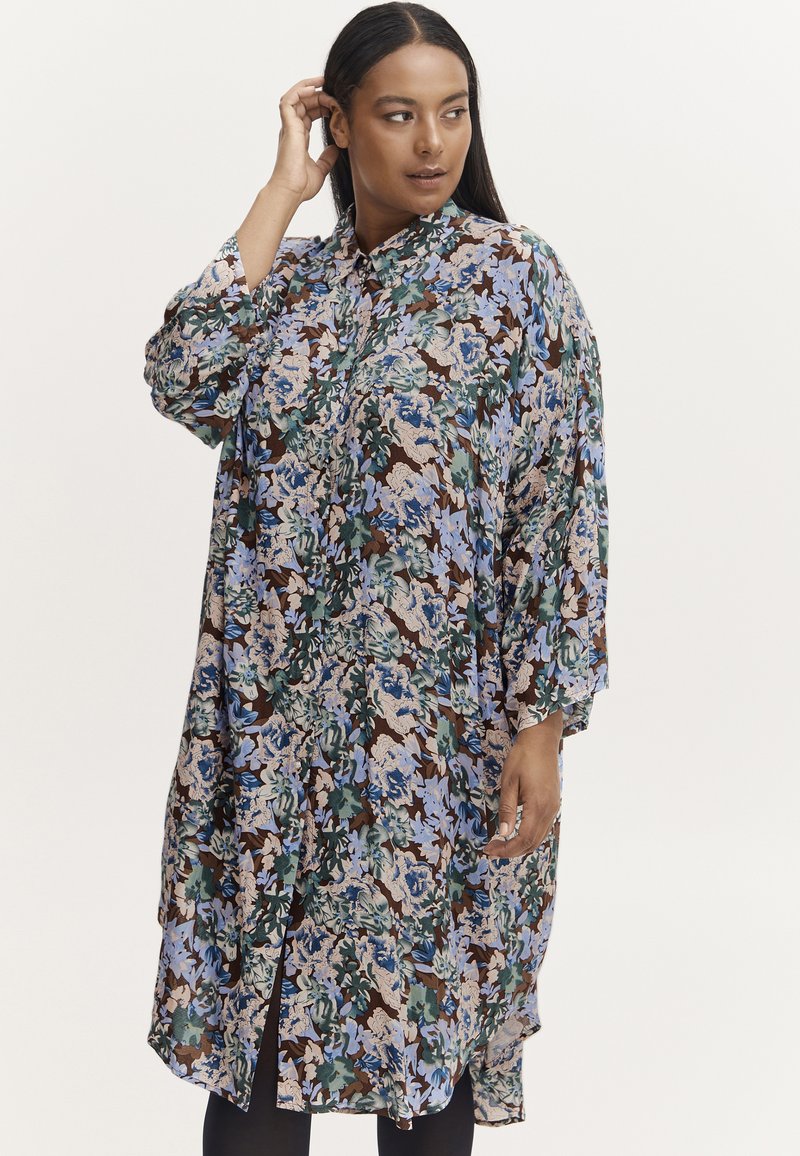 Sukienka koszulowa w kwiaty, z mieszanką niebieskich, zielonych i beżowych odcieni na brązowym tle, z zapięciem na guziki i luźnym, oversize'owym krojem.
