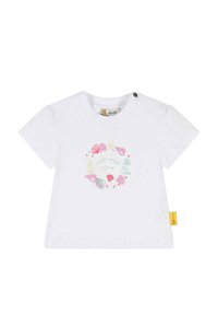 Camiseta de manga corta blanca con un diseño circular que presenta conchas marinas y el texto "verano" en colores pastel. Incluye un detalle de etiqueta lateral.