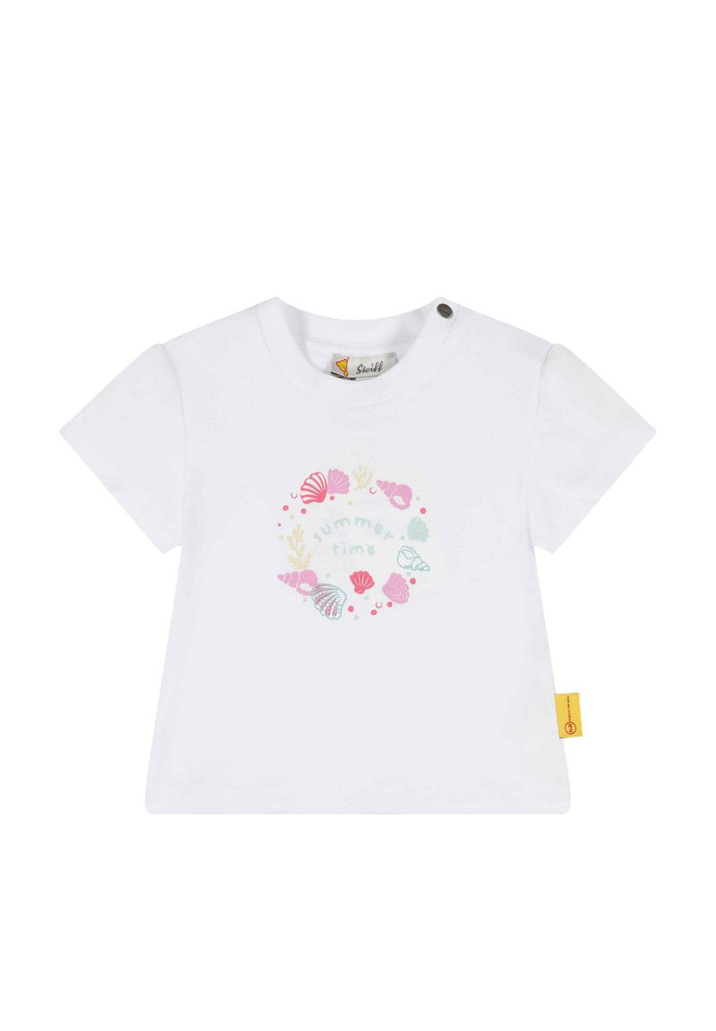 Camiseta de manga corta blanca con un diseño circular que presenta conchas marinas y el texto "verano" en colores pastel. Incluye un detalle de etiqueta lateral.
