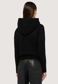 Felpa nera in maglia con colletto e polsini a coste, dotata di un cappuccio ampio. Abbinata a pantaloni in pelle nera per un look monocromatico.