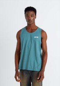 Teal katoenen tanktop met een ronde hals en het Levi's-logo in het wit, gecombineerd met donkerdenim jeans, wat een ontspannen pasvorm en een soepele textuur laat zien.