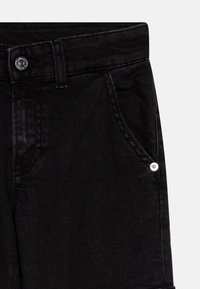 Vaqueros de mezclilla negra con una textura suave, que presentan un botón plateado y detalles en los bolsillos. La cinturilla incluye acentos de costura.