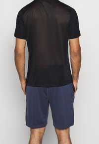Camiseta negra de manga corta con espalda de malla y corte relajado, combinada con pantalones cortos azul oscuro. Ambas prendas tienen texturas suaves.
