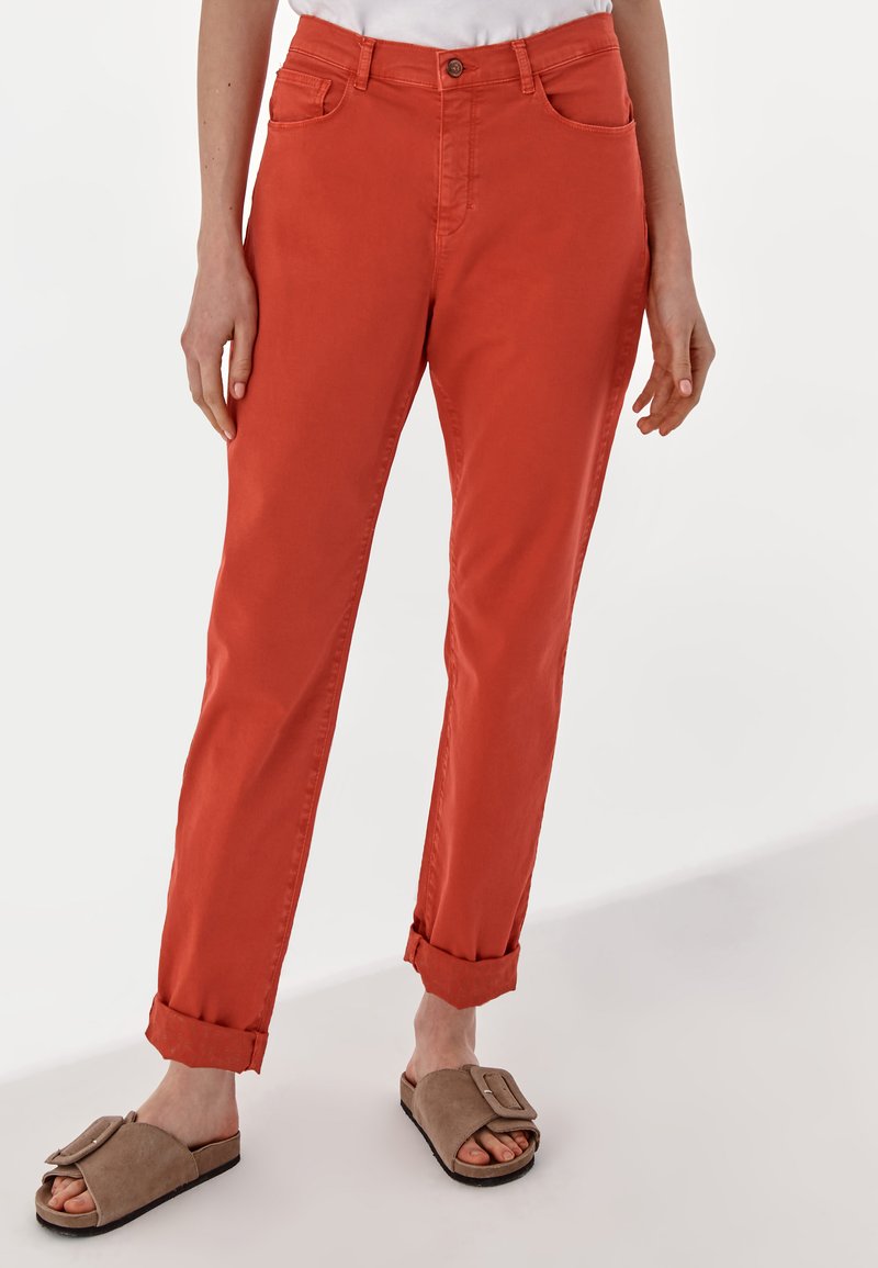 Orange, cuffed cotton pants with two front pockets and a single button closure, paired with brown slide sandals.
