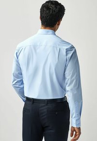 Helles blaues Hemd mit einer glatten Textur, langen Ärmeln und einem klassischen Kragen; kombiniert mit dunklen Hose, die über Gesäßtaschen verfügt.