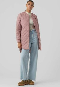 Giacca trapuntata rosa chiaro con colletto tondo, abbinata a un top beige a coste e jeans a gamba larga blu chiaro. Scarpe con tacco in tonalità beige completano l'outfit.