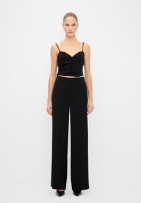 Top noir court avec des bretelles fines et un décolleté en cœur, assorti à un pantalon large noir taille haute. Tissu lisse, design élégant.