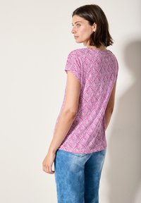 Haut à manches courtes en rose avec un motif de feuilles, fabriqué en tissu doux. Présente une coupe décontractée et est associé à un bas en denim bleu clair.