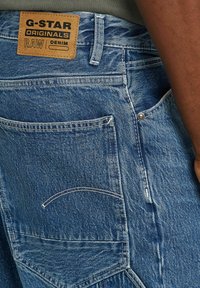 Niebieskie dżinsy z denimu z skórzaną metką z wytłoczonym napisem. Wyjątkowe detale to podwójne szwy oraz tylna kieszeń z krzywym szwem.
