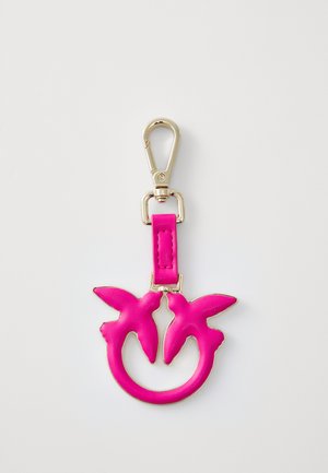 Portachiavi in pelle rosa con un design circolare che presenta due forme di uccelli. L'hardware in oro si attacca a una cinghia, esaltando il colore vivace e la texture.