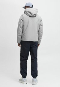 Grå isoleret jakke med hætte, parret med sorte bukser og grå sneakers. Har elastiske manchetter og snorejusteringer.