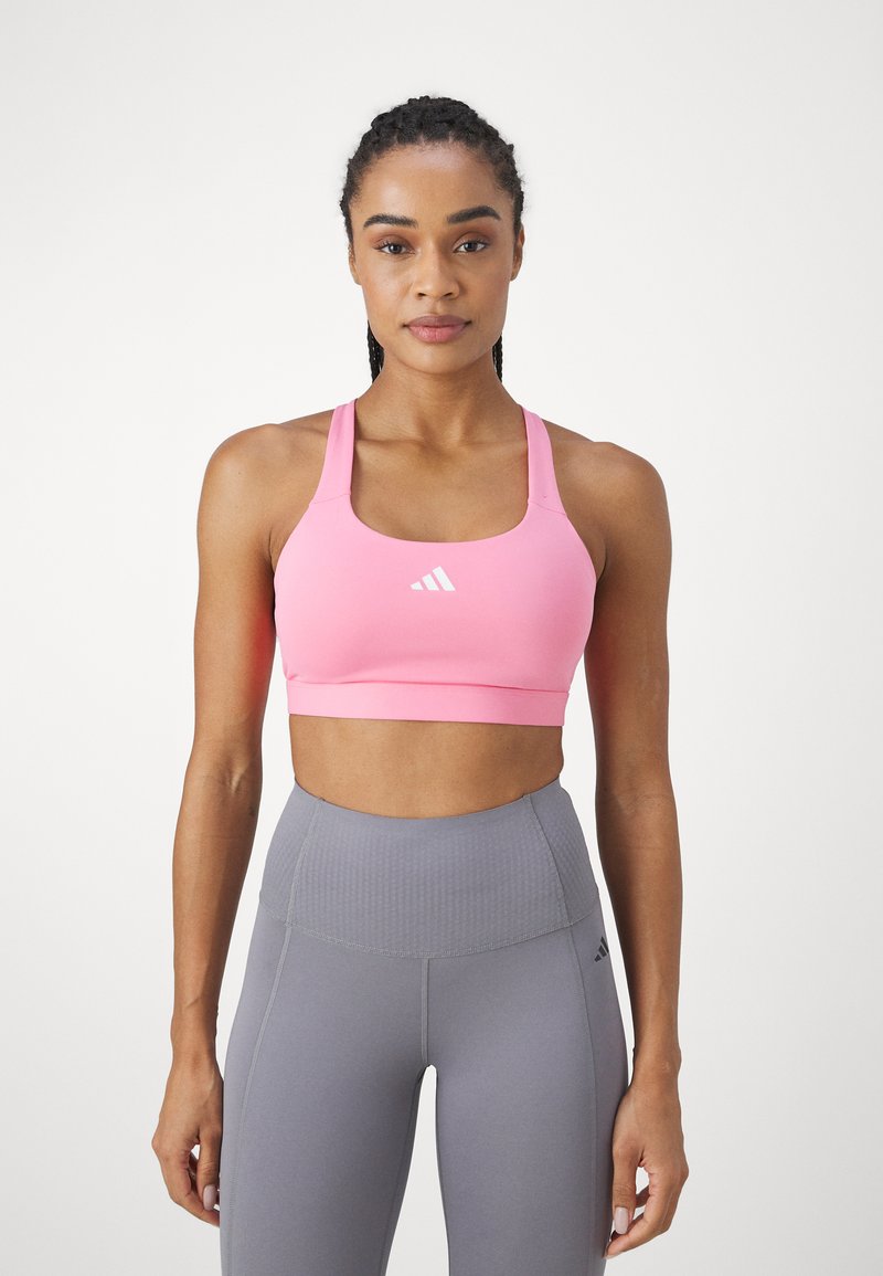 Rosa Sport-BH mit breiten Trägern und runder Ausschnittpartie, präsentiert mit einem weißen Logo. Kombiniert mit grauen, hochgeschnittenen Leggings mit strukturierten Details.