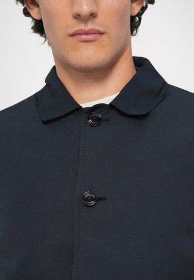 Marineblå jakke med krave, der har sorte knapper og synlige sømme. Glat tekstur med minimalistisk design uden mønstre.