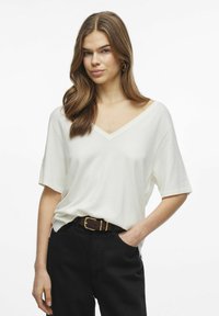 T-shirt bianco con scollo a V e maniche corte, realizzato in un tessuto morbido, abbinato a pantaloni neri a vita alta e una cintura marrone con fibbia dorata.