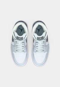 Baskets montantes grises et blanches avec un dessus en cuir et mesh, bout perforé, lacets plats, et un logo Jumpman sur la languette et la semelle intérieure.