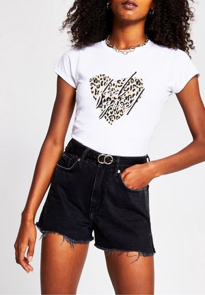 Woman wearing white t-shirt with leopard print heart and black text, paired with high-waisted black denim shorts with frayed hems and belt.