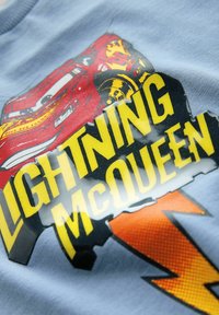 Modra bombažna majica z grafiko rdečega avtomobila in besedilom "LIGHTNING McQUEEN" v rumeni barvi, obogatena z oranžnim dizajnom strele.
