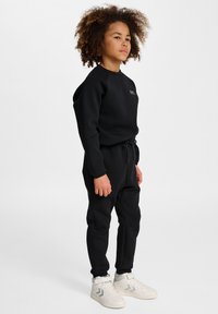 Zwarte hoodie met een ronde hals, geribde manchetten en bijpassende zwarte joggers met een trekkoord in de taille. Witte sneakers maken de outfit compleet.