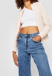 Ljust rosa bomberjacka med dragkedja fram och ribbade ärmar, tillsammans med högmidjade blå denimjeans med en klassisk femfickorsdesign.