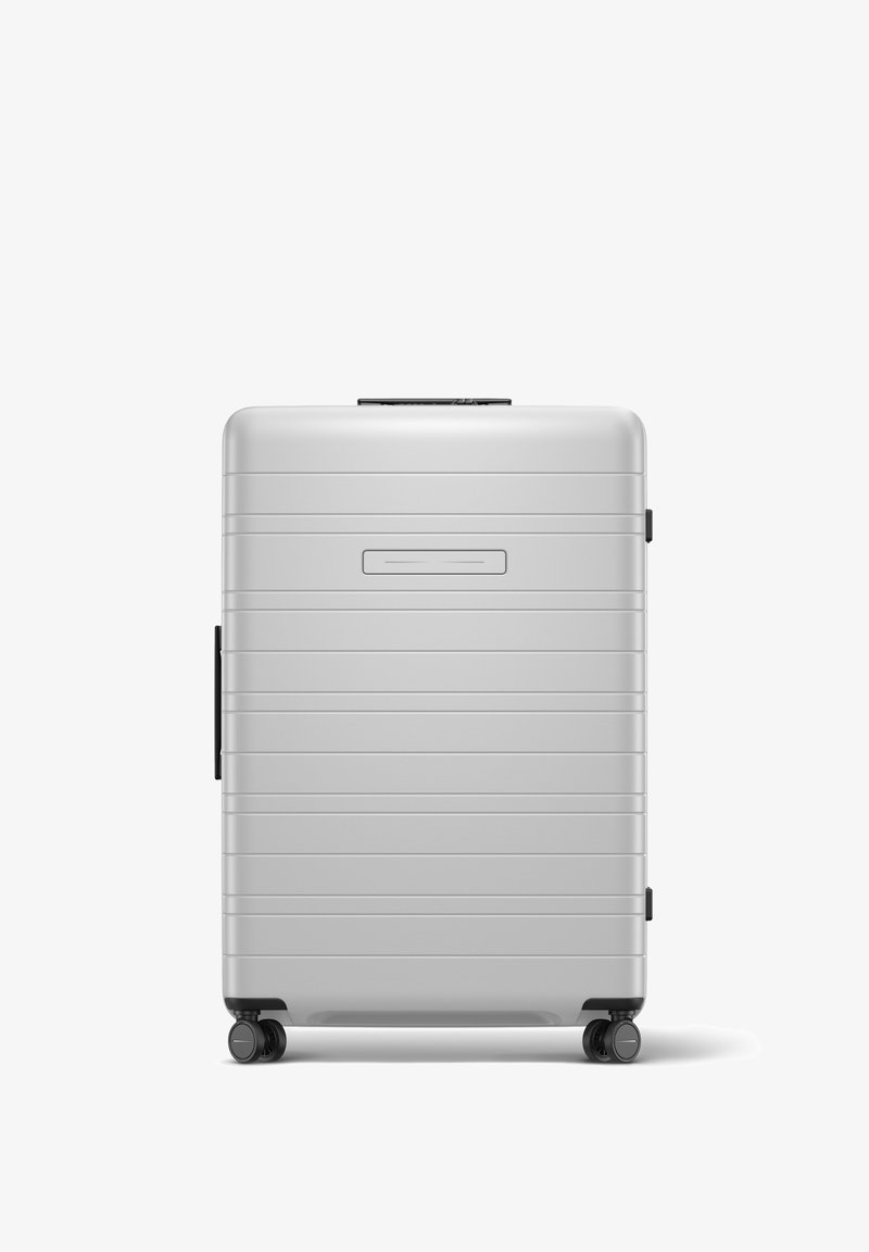 Silver hard-shell suitcase with vertical grooves, top handle, and four black wheels for mobility. Features a smooth texture and compact design.