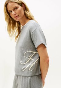 Szara bawełniana koszulka z krótkim rękawem i okrągłym dekoltem. Posiada dużą, kremową, stylizowaną grafikę "FH" z boku.