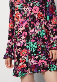 Vestido floral negro con vibrantes patrones en rosa, rojo y verde. Cuenta con mangas largas con puños con volantes y un dobladillo con volantes en capas.