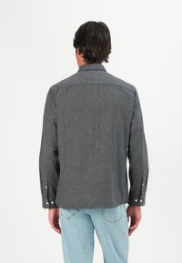 Grå teksturert skjorte med lange ermer, knappelister og krage. Enkelt design med avrundet falden og detalj på bakre rygg.