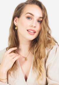 Gouden sieradenset met een hangerketting en oorringen met een cirkelvormig K-logo ontwerp. Zachte, gestructureerde achtergrond.