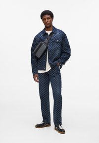 Sötétkék farmerdzseki és nadrág houndstooth mintával, fekete crossover táskával és fekete edzőcipővel, fehér fűzővel.