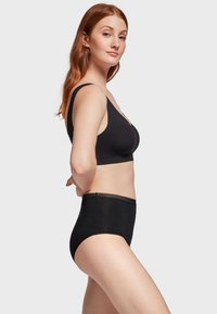 Soutien-gorge sans fil noir à décolleté en scoop et larges bretelles, associé à des culottes noires taille haute avec un délicat bord festonné.