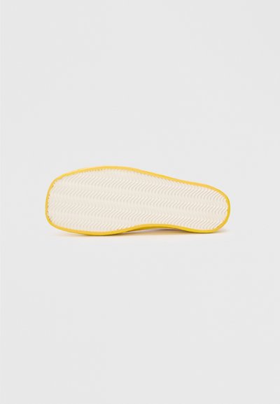 Rubber shoe sole with a textured white surface and a bright yellow border. Patterned grooves for traction are visible on the bottom.