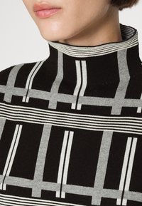 Pull à col roulé noir et gris à motifs, avec des rayures verticales et horizontales, présentant un col haut côtelé et une texture en maille douce.