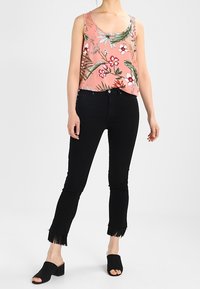 Débardeur rose à motif floral avec des feuilles vertes, associé à un jean noir aux ourlets effilochés et des chaussures noires à enfiler.