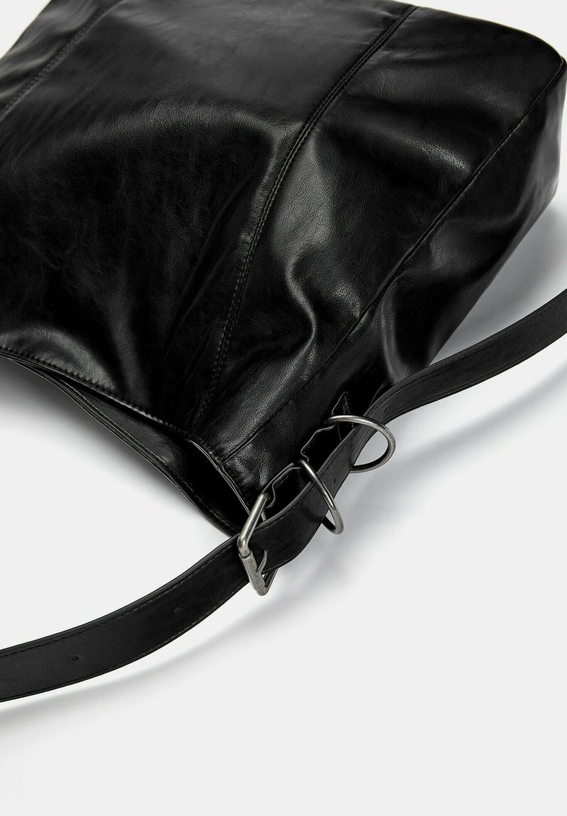 Bolso de hombro de cuero negro con hebilla plateada y detalles en la correa sobre un fondo blanco.