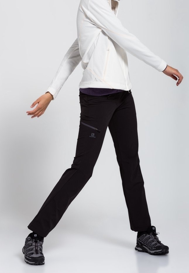 Svarta utomhusbyxor med en ficka med dragkedja, kombinerade med en vit jacka. Byxorna är något smalare i benen och är designade för atletisk användning.