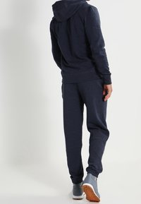 Sudadera azul marina y joggers a juego, hechos de tela suave, con capucha ajustable y puños de canalé, combinados con zapatos deportivos grises.