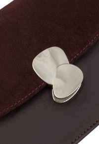 Clutch in suede borgogna con una chiusura tonale in argento liscia, caratterizzata da un motivo testurizzato e bordi in pelle scura a contrasto.