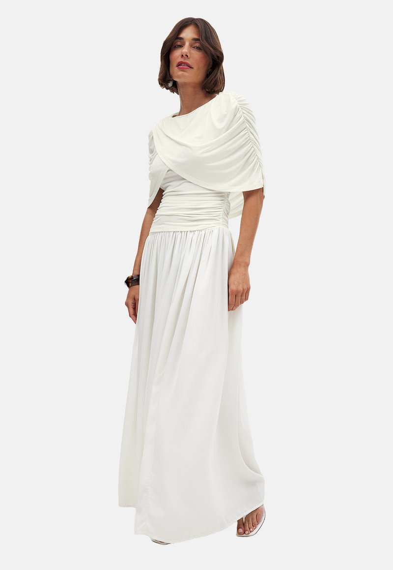 White, floor-length dress made of soft fabric. Features a draped bodice with pleats and a fitted waist, flowing skirt, and short sleeves.