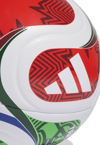 Zbliżenie na białą pi�łkę nożną z czerwonymi, zielonymi i niebieskimi wzorami oraz czerwoną logo Adidasa z trzema białymi paskami.