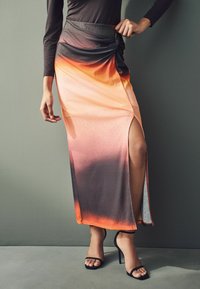 Jupe longue à dégradé de couleurs allant de l'orange au gris, avec une fente haute sur le côté gauche et une taille nouée. Accompagnée de sandales à talons hauts noires.