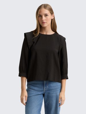 Haut noir avec des manches courtes et structurées, présentant un col rond et un tissu texturé. Associé à un jean en denim bleu clair.
