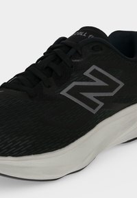 Μαύρο και γκρι αθλητικό παπούτσι New Balance με μαύρα κορδόνια και παχύ λευκό πέλμα, εμφανιζόμενο από μπροστινή πλευρική γωνία.