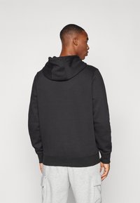 Sort pullover hoodie med en kænguru-lomme, ribbede ærmer og kant, samt en hætte med snore; båret sammen med grå cargo-bukser.