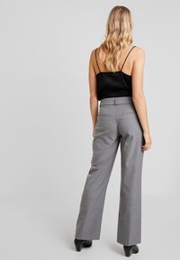 Šedé kalhoty s širokými nohavicemi a přizpůsobeným střihem, s hladkým povrchem, poutky na pásek a dvěma zadními kapsami. Kombinováno s černým topem bez rukávů.