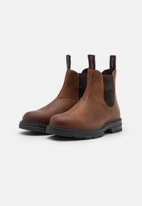 Bottines en cuir marron avec des panneaux latéraux élastiques, des poignées de traction et des semelles en caoutchouc. Le design présente une finition lisse et une branding discrète.